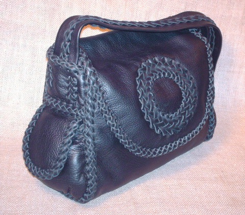  This custom and handmade purse was made with Black moccasin cowhide leather and constructed by braiding 1/4" wide laces of the same material. All of it seams are braided, as well as, the edges of the flap/s, down the center/length of the strap, and the circle applique on the flap. 
