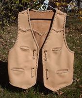  This custom leather vest was hand made in the USA for the buyer. Made of moccasin cowhide, it features front pointed yokes, a back pointed yoke, two slit breast pockets (credit card size), two slit hip pockts, and with four sets of 'trick braid' straps for snap closures. It also has (what I call) a back/bottom draft flap. 