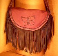  The woman that purchased this bag wanted it very elaborate. It has fringe hanging from the flap and from the two side pockets. The long flat strap employs three lengths of braiding - one down the center and edge braiding along each side of it. 