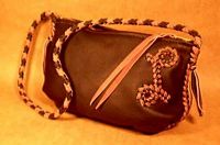  This purse was made with a Black leather body that was constructed with two-tone, Black and Chestnut, leather braiding. This includes it's seams, strap, and the capital letter 'L' on it's side. Like all the bags of this style, it has pleats in it's bottom corners that give it dimension. 