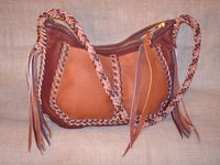  This large two-toned leather bag has a 12" zipper closure, and a large divided pocket. The long round, 8 strand braided strap has quite long tassels hanging from the ends of it. 