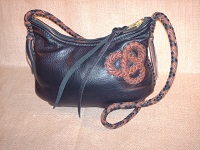  A Black and Mahogany bag with a Mahogany tri-loop applique on one side of it. The same two colors are used for the strap which has short tassels. 