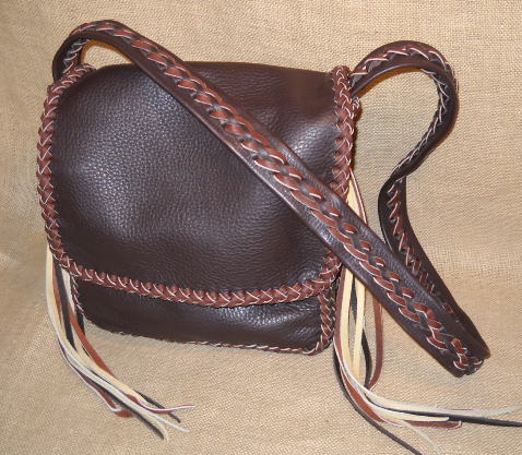 This two-tone custom handmade leather purse was built to carry an Apple Ipad - it has an inside back pocket that the pad slips into. It's over-all dimensions are about 10" wide by 10" high by 4.5". It's completely built using various ways of elaborate braiding. The 1/4" wide lacing is cut from the same 4 oz. moccasin cowhide leather that the bag is made with. All of the seams are joined with an applique braid. That same braid is used down the center/length of the strap. The flap has an edge braid around it. The strap is fastened to the body with braiding and has very long tassels that hang from it.   The two colors of leather that this bag is built with are dark Brown and Mahogany. Some of the tassels are of the color Cream.   There are two compartments under the flap of this bag. 