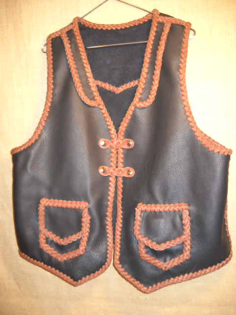  This two tone vest is built with moccasin cowhide leather including for the braided lacing. It has front lapels, a back pointed yoke, patch hip pockets with flaps and two sets of snap closures braided with what is called a 'trick braid'. 