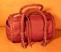  This small Mahogany colored barrel bag has a large brass zipper and is about 7" long with a 5" diameter. It has two 8 strand round braided handles with short tassels hanging from the ends of them. 