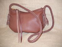 This Mahogany colored leather bag has a large #10 YKK zipper that has leather attached to the slide. It has braided seams and an 8 strand braided strap that has short tassels hanging from it. 