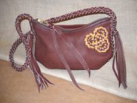  These two pictures are of a small Mahogany colored leather shoulder bag with seams that are elaborately braided. It has an 8 strand braided strap with 8 long tassels that hang from each end of it. It has a two-toned Celtic tri-loop knot braided on the side of it. 