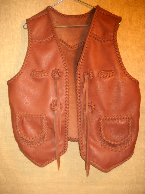  A rather Western style braided vest using moccasin cowhide leather. It has pointed front yokes, a pointed back yoke, two patch hip pockets with flaps, ans two breast pockets (credit card size). It also has straps hanging from a conchoe I fashion with a braided circle. 