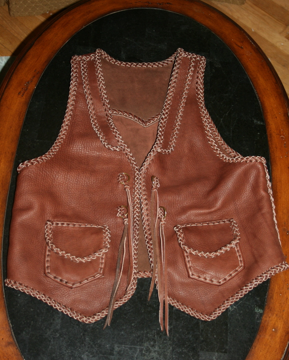  This rather Western style braided leather vest features front lapels, a back pointed yoke, patch hip pockets with flaps, and straps with solid brass D rings. 
